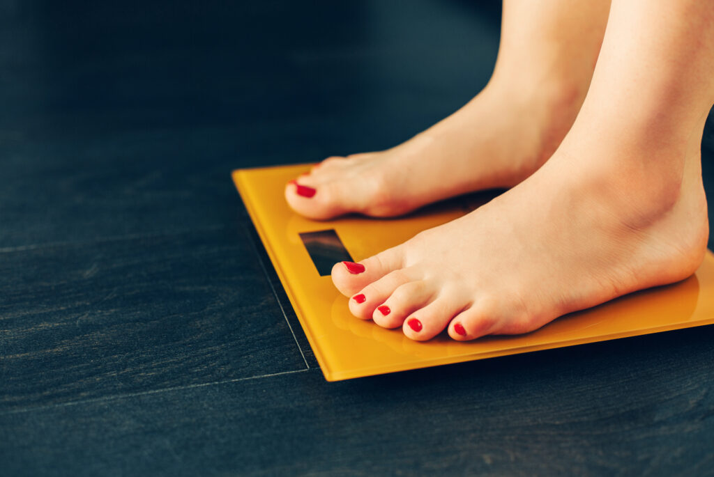 True Medical Weight Management 2 Feet on an orange scale against a dark floor, representing medical weight management