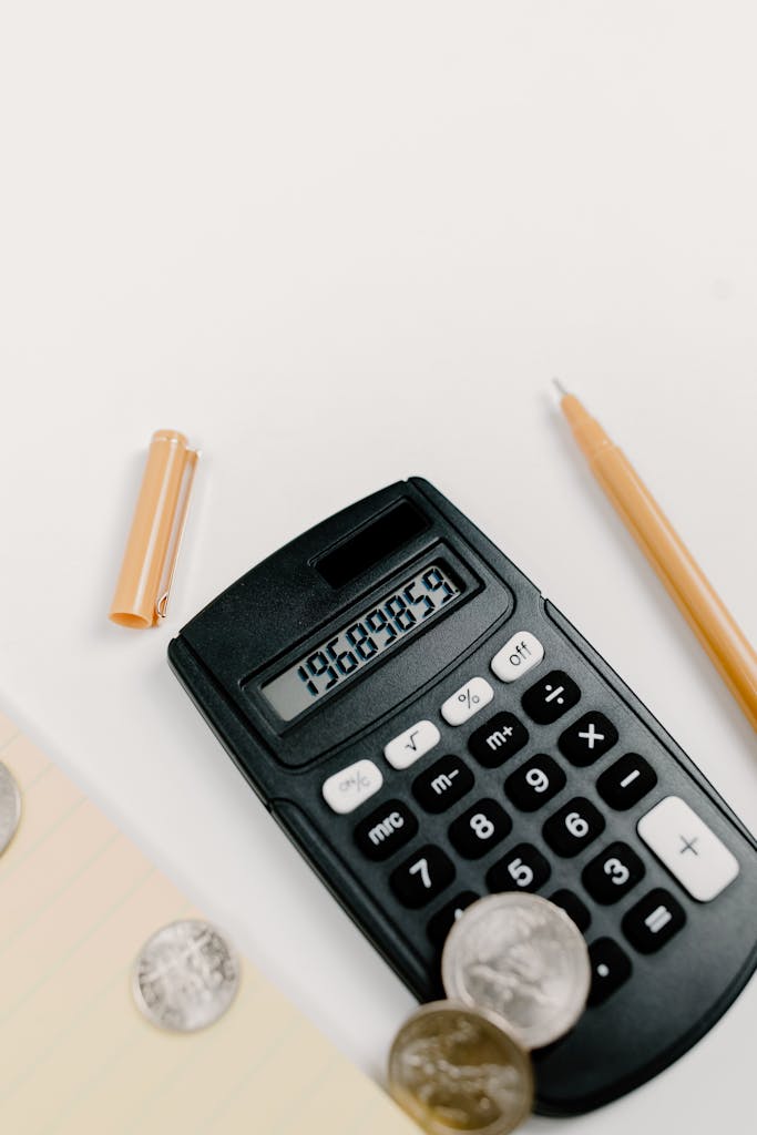 Black calculator with coins and office supplies on white surface
