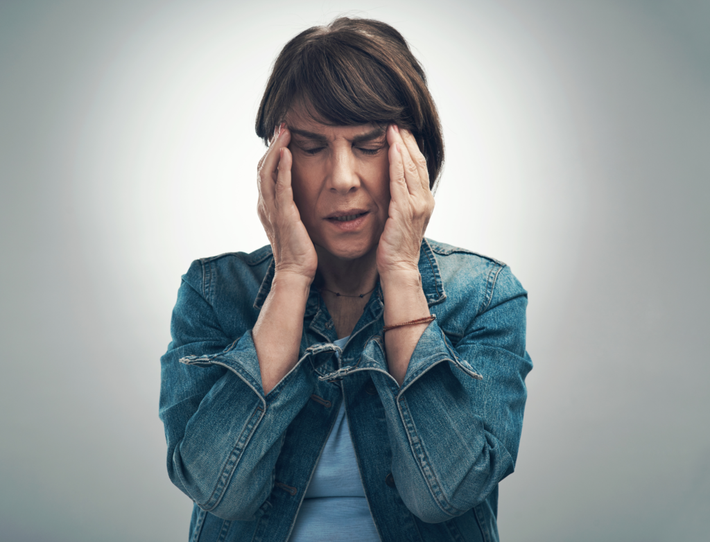 The Silent Fire in Your Brain: Neuroinflammation 2 Middle-age woman with a headache, holding her hands to her temples, representing neuroinflammation